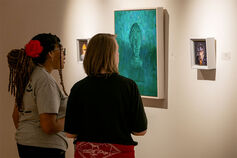 Two students in the art gallery discussing one of several portraits displayed on the wall.